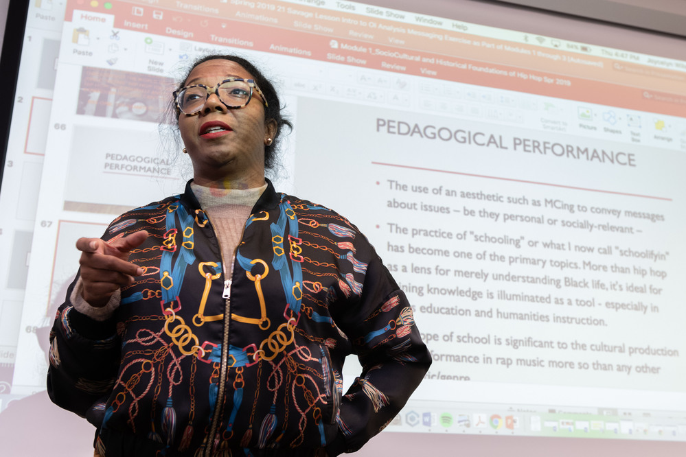 instructor at the front of a class with a slide show behind them